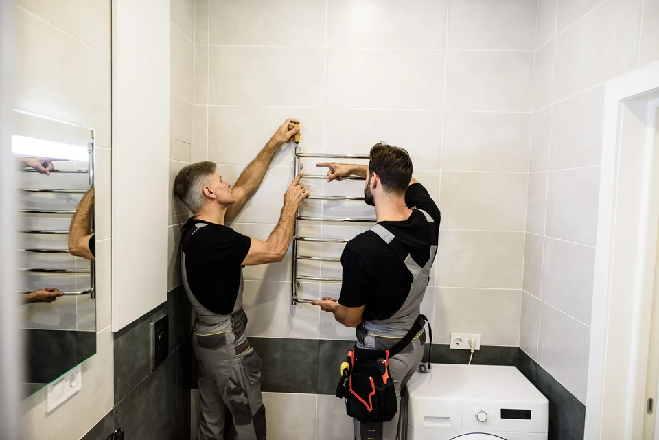 Photographie d'une équipe de 3 à 4 professionnels du chauffage, climatisation et plomberie en tenue de travail (combinaison bleu marine ou vêtements professionnels aux couleurs Paineau Tortevoie) posant ensemble devant un véhicule utilitaire blanc de l'entreprise. Les collaborateurs affichent une expression confiante et bienveillante, suggérant la cohésion et l'écoute client. Un professionnel pourrait tenir des outils ou équipements (tournevis, clé à molette, thermomètre d'ambiance) symbolisant les différentes compétences. L'arrière-plan montre un chantier ou un local technique flou, contexte professionnel authentique. Éclairage naturel, ambiance professionnelle et positive.