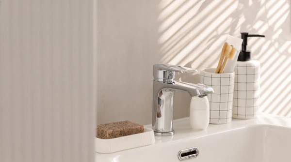 Photo professionnelle en plan d'ensemble d'un plombier portant un uniforme de travail bleu ou blanc marqué du logo de l'entreprise, installant ou entretenant une canalisation en cuivre ou PVC sur un mur intérieur. L'artisan doit être actif, par exemple serrant une connexion avec une clé à sertir ou un clé anglaise, ou raccordant des tuyauteries visibles. L'arrière-plan doit montrer un environnement résidentiel authentique (murs, appareillage sanitaire en arrière-plan) sans surcharge visuelle. La lumière naturelle ou professionnelle doit mettre en avant le geste métier. Image de qualité photographique professionnelle, sobre et représentative du métier artisanal de plombier.